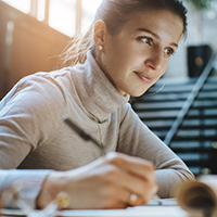 A woman looking at a laptop screen and writing A woman looking at a laptop screen and writing