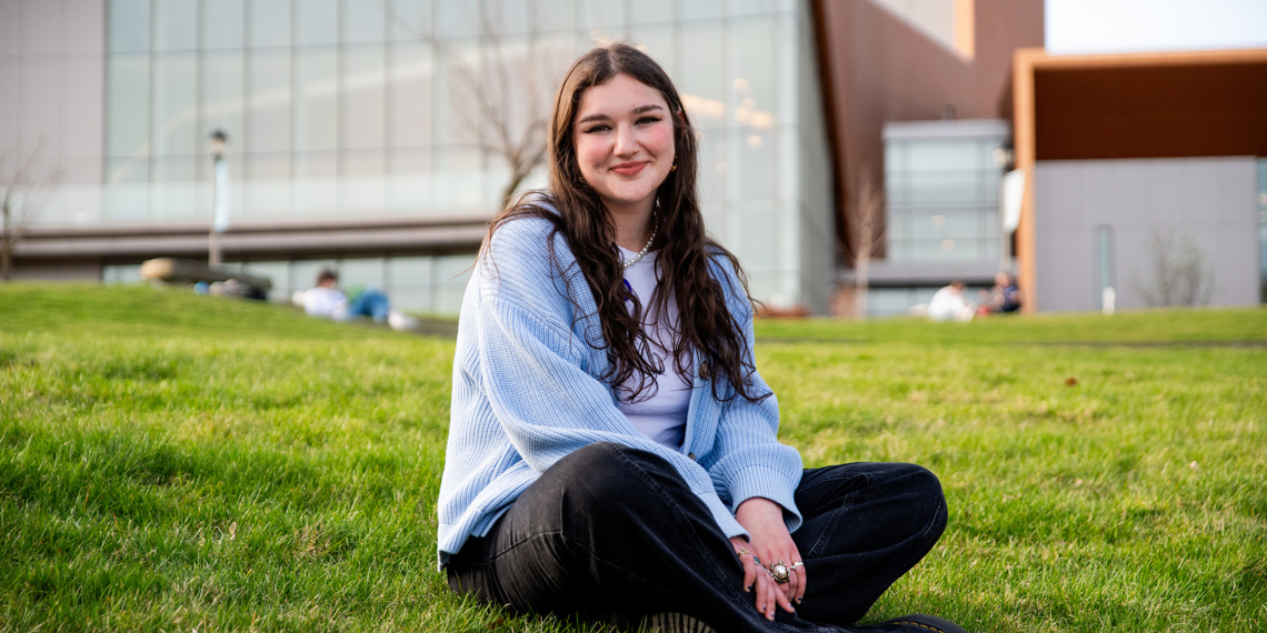 Senior Sydney Baltuck sitting cross legged outside the Myrtle Woodson Performing Arts Center.