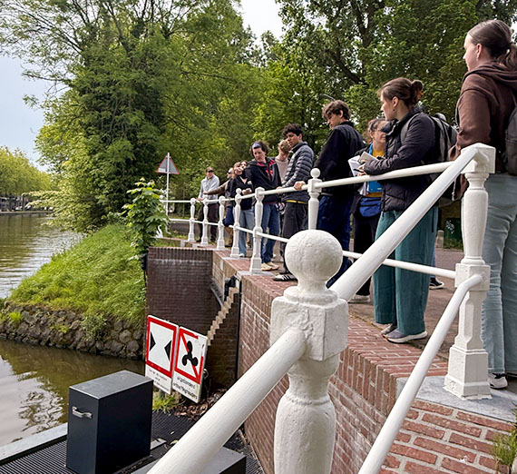 Students stand along a white railing looking into a canal.