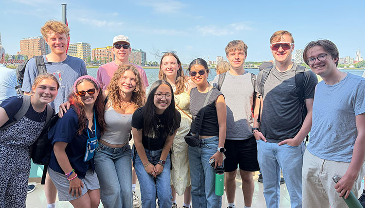 11 young people stand in the sun with the skyline of a European city behind them