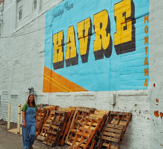 Environmental Studies & Sciences Alumna Hanna Gangwish in front of a Havre, Montana logo painted on a wall.