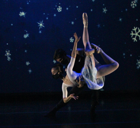 Two masked dancers, one holding the other up while she poses with legs pointing to the ceiling. Background is blue with snowflakes. Two masked dancers, one holding the other up while she poses with legs pointing to the ceiling. Background is blue with snowflakes.