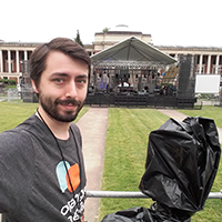 Steven poses with a camera at an outdoor event. Steven poses with a camera at an outdoor event.