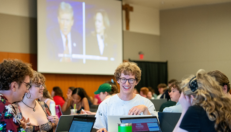 students sitting at tables watching the presidential debate on big screens students sitting at tables watching the presidential debate on big screens