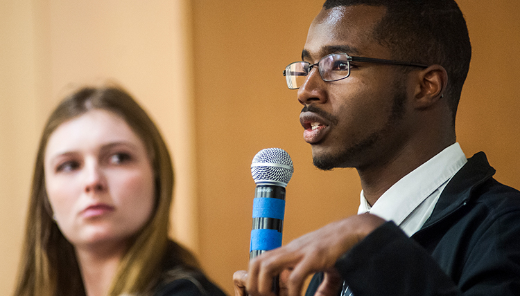 Caleb Dawson speaking into microphone while another student looks on Caleb Dawson speaking into microphone while another student looks on