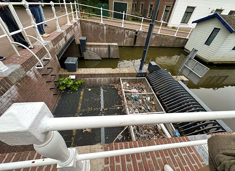 A large net catches trash from the water in a canal.