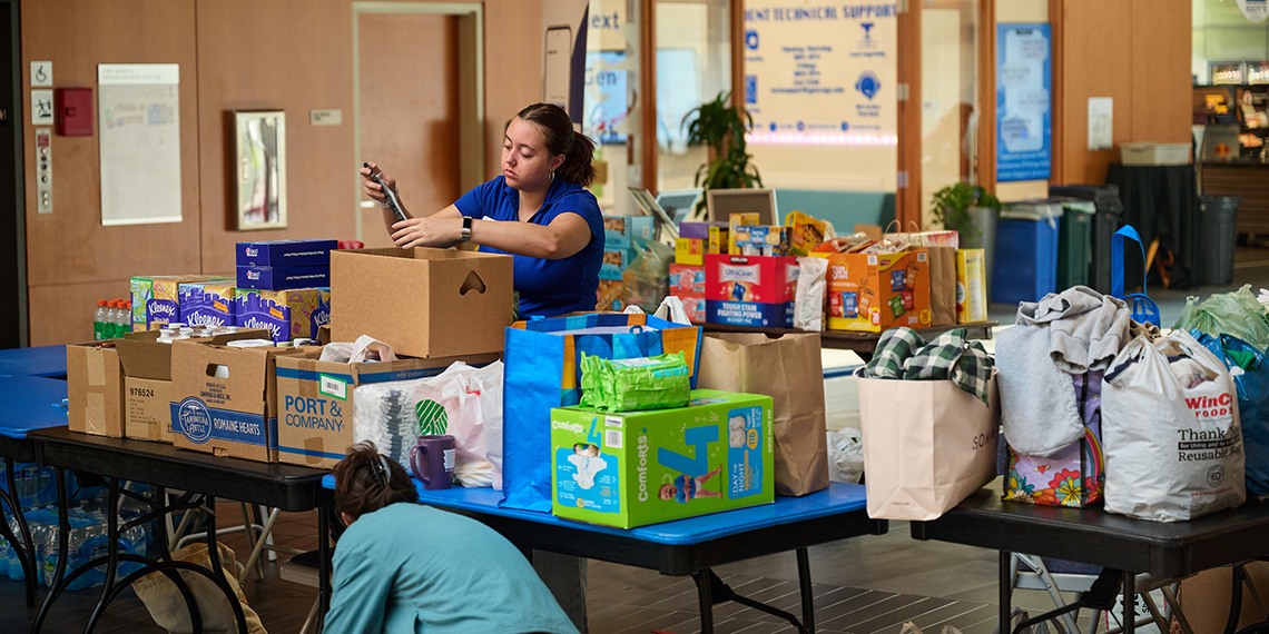 A woman stands among tables piled with household items