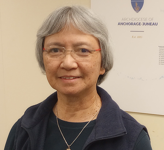 woman with short grey hair wearing a black fleece vest over a black long sleeve shirt and a cross necklace