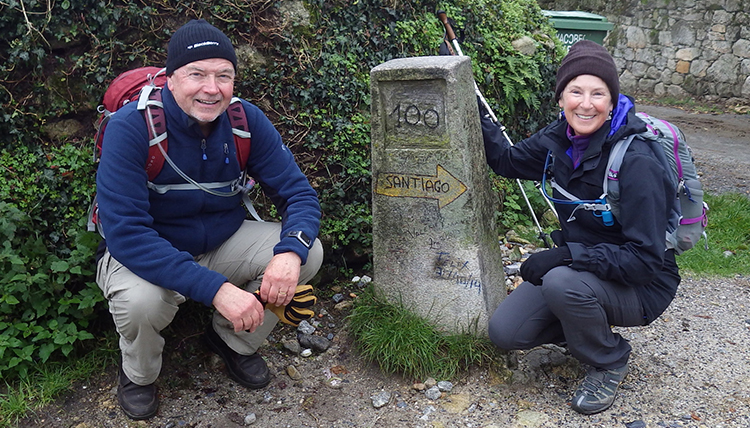 a couple kneels beside a mile marker on the Camino de Santiago a couple kneels beside a mile marker on the Camino de Santiago