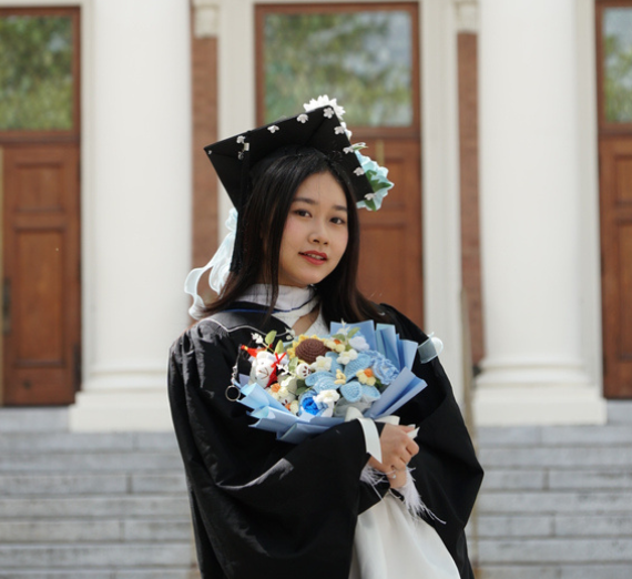 Thi Ngoc My Le stands with flowers in graduate attire.