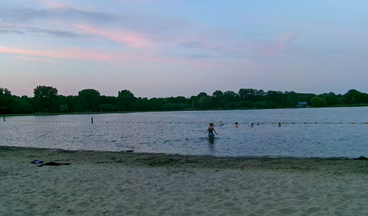 Students play in shallow water of a beach under a sunset sky