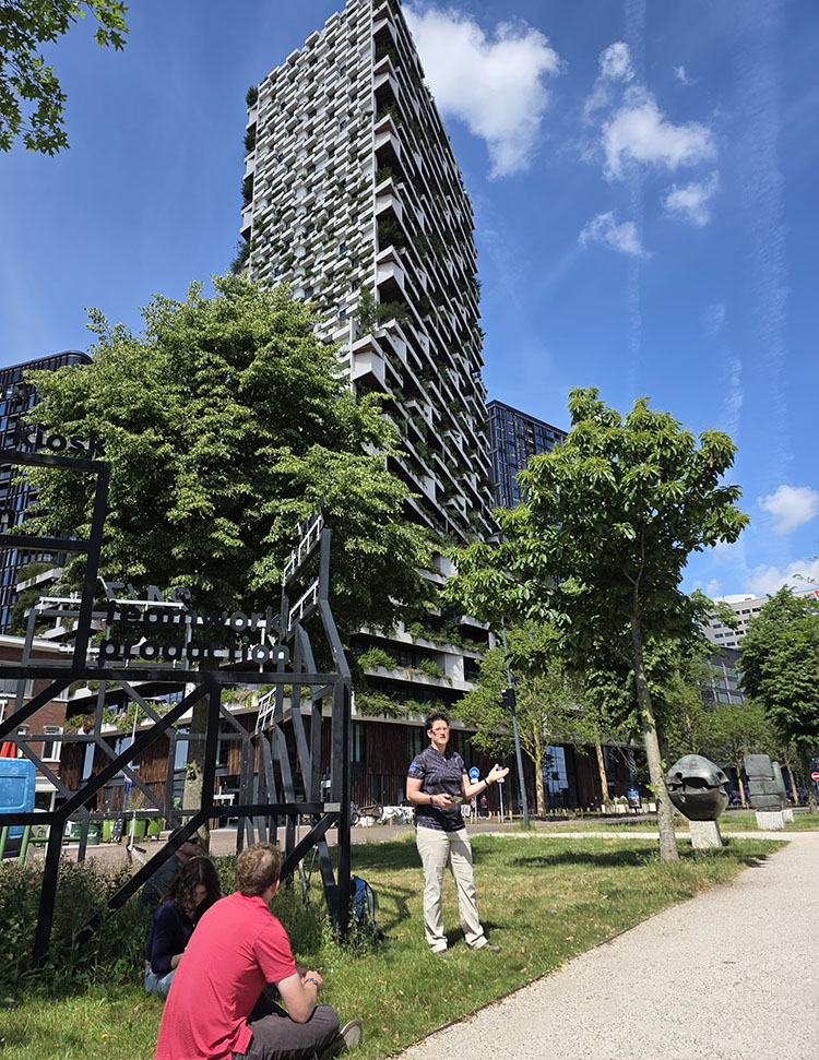 Woman speaks on the grass outside a tall building dotted with green growth