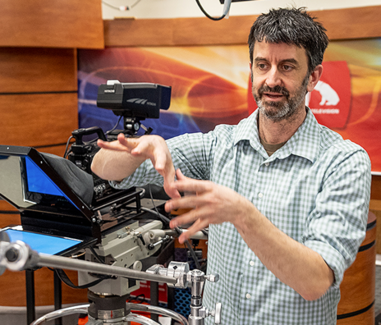 Dr. Matt McCormick instruction in the film studio next to a video camera.