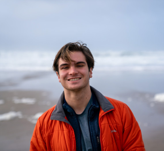 A picture of a student in a orange jacket standing on the beach