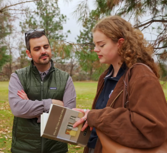 A philosophy professor and student outside in discussion, the student is holding a book.