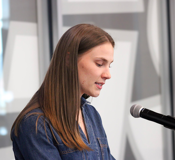 A woman with long dark hair speaks at a microphone