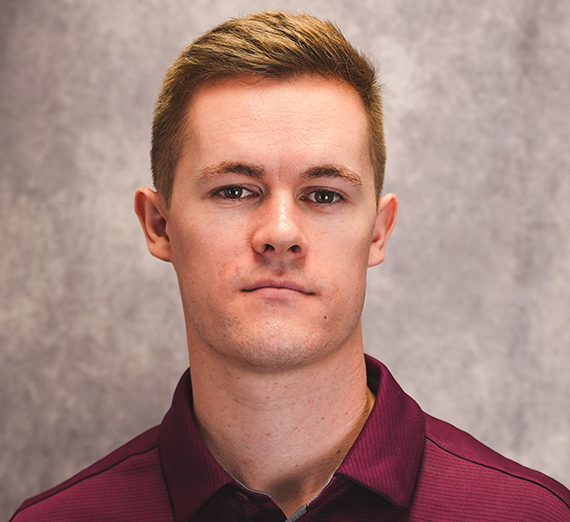 person with short hair and red polo standing in front of a neutral background. The photo is close up of the person's face.