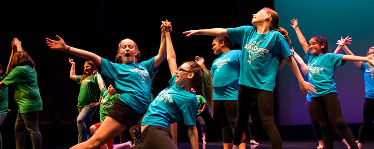 Several childen in matching blue shirts dance as a group. Several childen in matching blue shirts dance as a group.