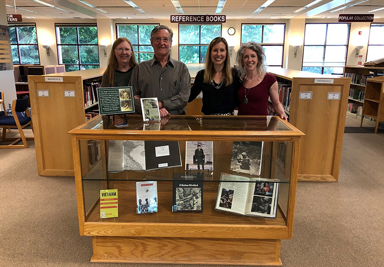 Group photo of Larry Plager and the Telling War group gathered around a bookcase with a collection of Vietnam war books. Group photo of Larry Plager and the Telling War group gathered around a bookcase with a collection of Vietnam war books.