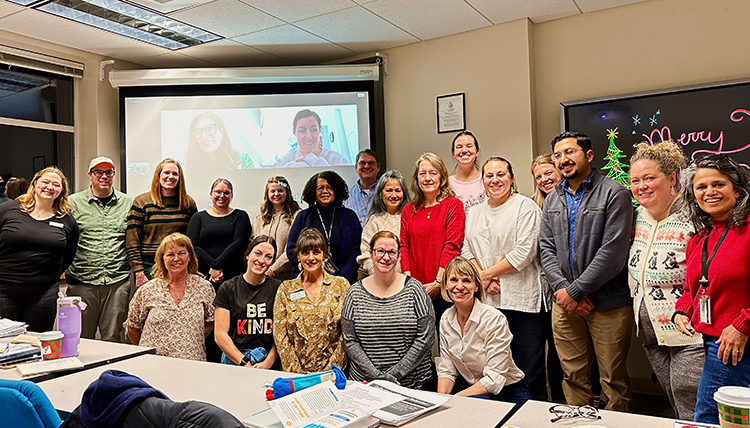 A group of people stand in front of a screen in a classroom A group of people stand in front of a screen in a classroom