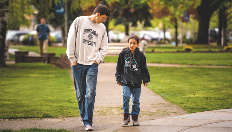male college student walks outdoors with middle school student male college student walks outdoors with middle school student
