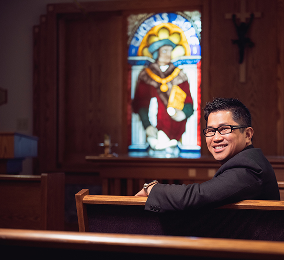 A man sitting in a church pew in front of a stained-glass window