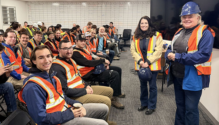 Many young adults sitting in rows wearing safety vests with two women on the right of the frame Many young adults sitting in rows wearing safety vests with two women on the right of the frame