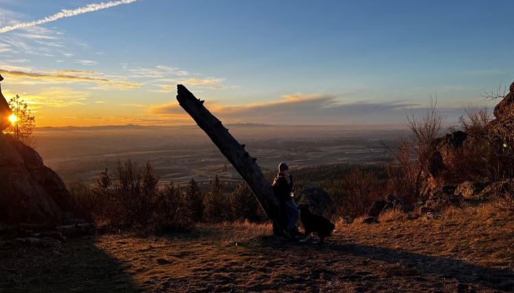 A boy and a dog sitting watching the sun rise from a hiking trail in Spokane, WA A boy and a dog sitting watching the sun rise from a hiking trail in Spokane, WA