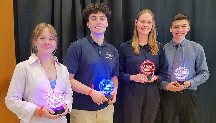 Expo 20 CE 2026-0429_193351-bd Four students stand in front of a black curtain with glowing trophies