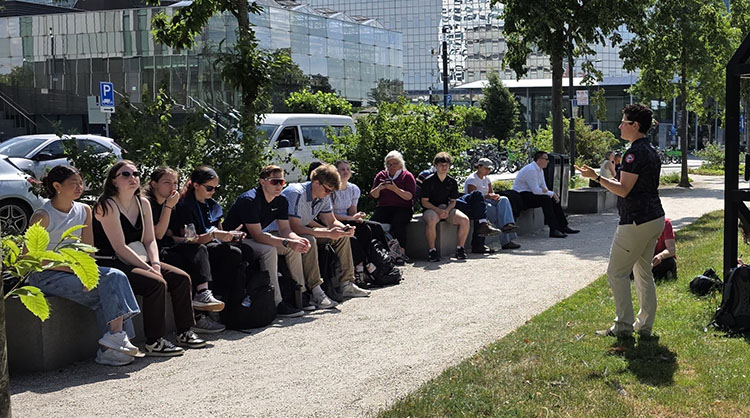 delft 2026-0601 wonderwoods lecture-bd Teacher addresses a dozen students sitting on a low wall outdoors