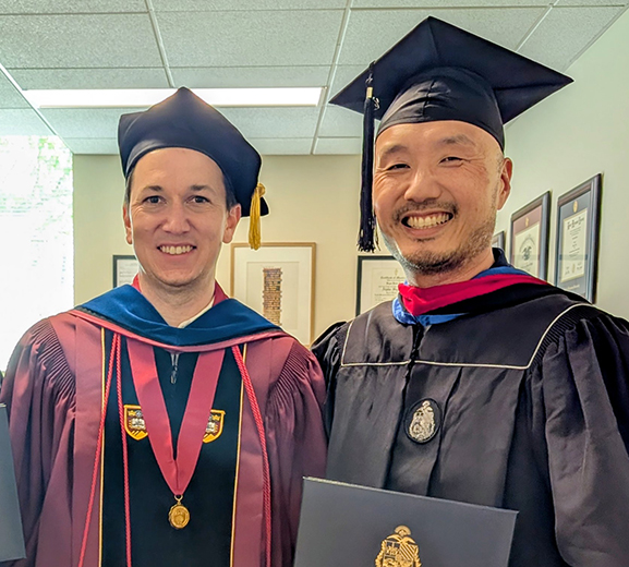 Dr. Kevin Brown on the left, man with doctoral attire and on the right is Andrew Lee, man wearing graduation attire and holding diploma