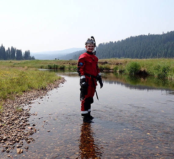 Will Gillick stands in the middle of a stream.