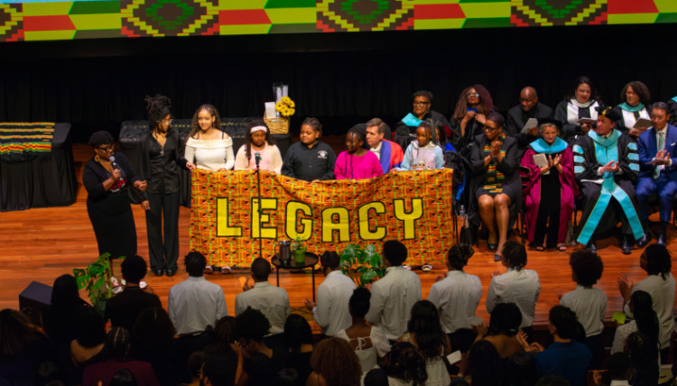 Students on stage hold a banner that reads 
