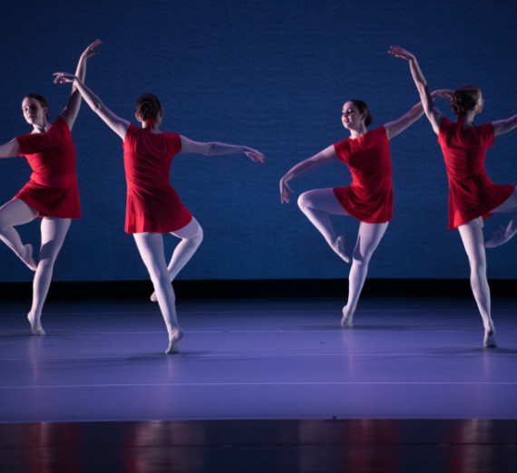 Four dancers in red dresses and white tights dancing in a cirle with arms in the air, against a blue background. Four dancers in red dresses and white tights dancing in a cirle with arms in the air, against a blue background.