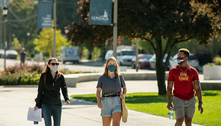 Three people walk through campus with masks. Three people walk through campus with masks.