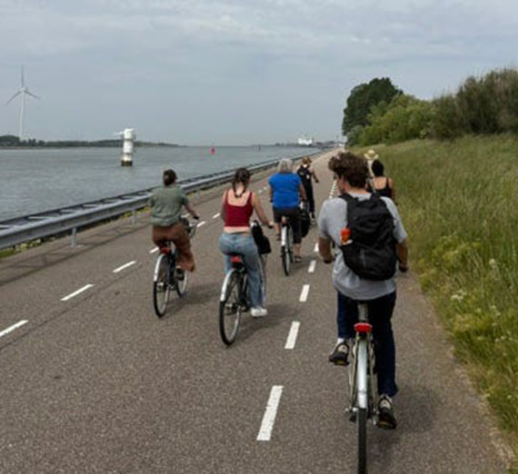 A group of five students and a teacher ride down a road next to a waterway