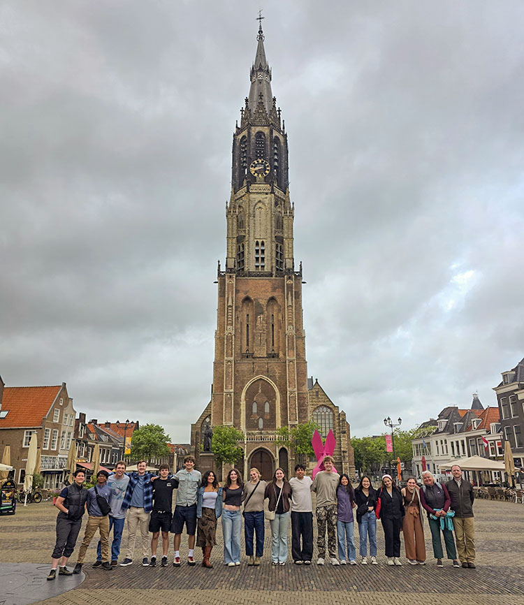 18 people of various ages stand in front of a very tall European church