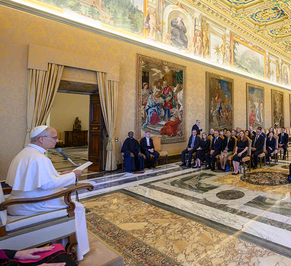 The seated pope talks to a room of seated guests at the Vatican