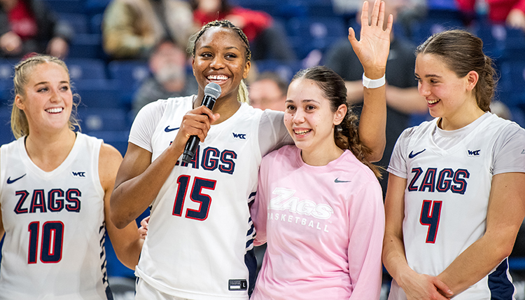Four women basketball players are celebrated on Senior Night, one holding a microphone and talking Four women basketball players are celebrated on Senior Night, one holding a microphone and talking