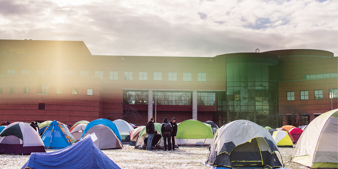 Three students stand outside of their tent surrounded by tents
