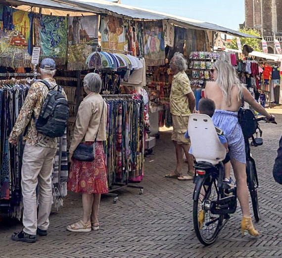 Scattered shoppers on foot and bicycle peruse stalls at an open-air market