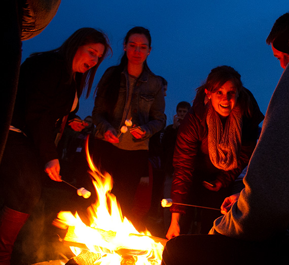 Students gathered around a campfire roasting marshmallows. Students gathered around a campfire roasting marshmallows.
