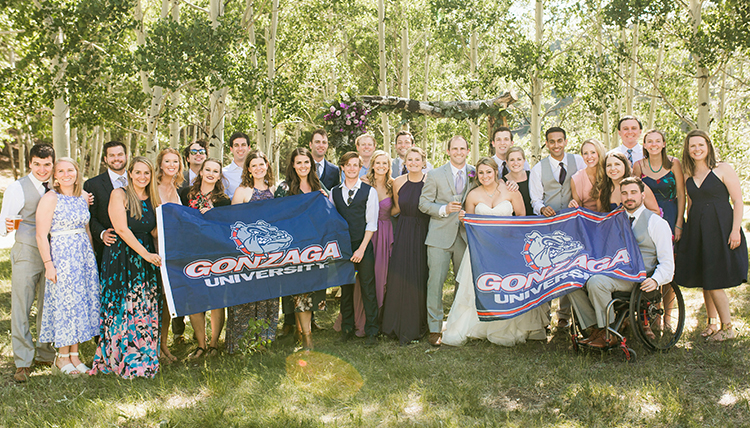 A group of wedding guests standing outside, holding two Gonzaga University flags. A group of wedding guests standing outside, holding two Gonzaga University flags.