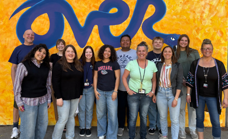 A group of students posed in front of a bright yellow wall. A group of students posed in front of a bright yellow wall.