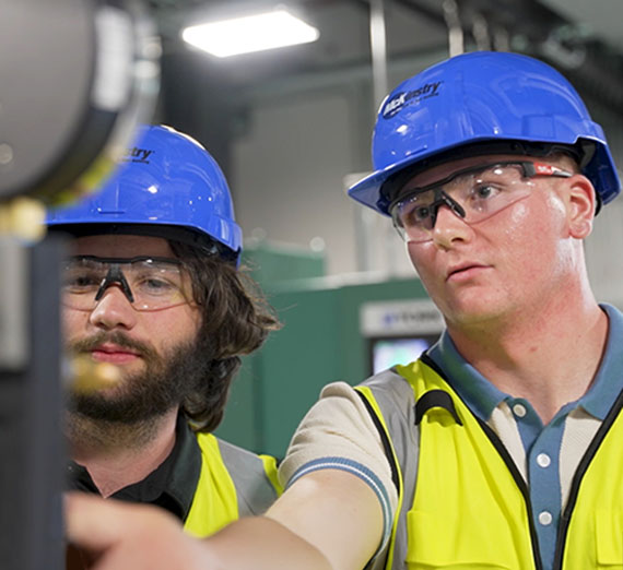 Two young men in safety equipment working on industrial machines.
