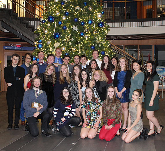 Large group of students posed for a photo in front of a decorated Christmas tree. Large group of students posed for a photo in front of a decorated Christmas tree.