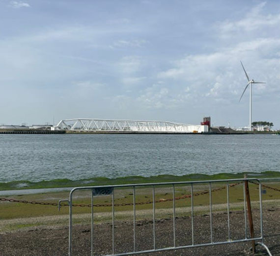 In the distance across a large waterway, a low white barrier sits next to a modern windmill