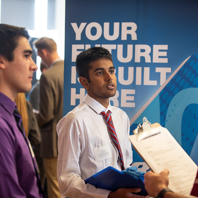 A young man wearing a white dress shirt and red tie listens to an employer representative at the All Majors Career Fair. A young man wearing a white dress shirt and red tie listens to an employer representative at the All Majors Career Fair.