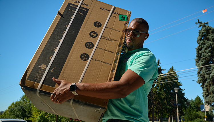 A man wearing a teal t-shirt carries a large box A man wearing a teal t-shirt carries a large box