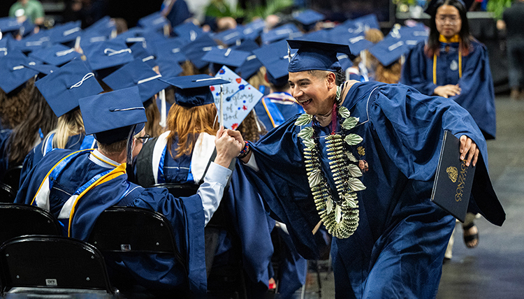 A graduate high-fives his peers as he runs down the aisle at commencement A graduate high-fives his peers as he runs down the aisle at commencement